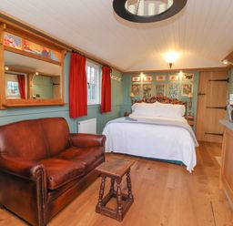 A bedroom with a double bed a brown leather sofa a small wooden table and red curtains at Arts and Crafts in Bolton Percy near Tadcaster