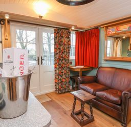 A living room with a brown leather sofa a small wooden table and a champagne bucket on a countertop at Arts and Crafts in Bolton Percy near Tadcaster