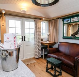 A small living area with a brown leather sofa a wooden stool a corner table with a lamp and double glass doors leading outside at Amy Johnson in Bolton Percy near Tadcaster