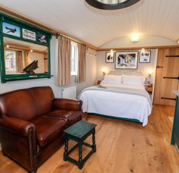 A bedroom with a leather sofa a bed and a green framed mirror at Amy Johnson in Bolton Percy near Tadcaster