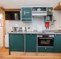 A kitchen with green cabinets a sink an oven a TV and kitchen utensils at Amy Johnson in Bolton Percy near Tadcaster