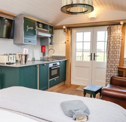A kitchen area with green cabinets a sink an oven a television and a wooden chair near glass doors at Amy Johnson Bolton Percy near Tadcaster