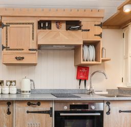 A kitchen with wooden cabinets a countertop with a kettle and jars a sink a faucet an oven and plates at The White Princess Bolton Percy near Tadcaster