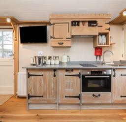 A kitchen with wooden cabinets, a sink, oven, kettle, toaster, and a mounted television at The White Princess in Bolton Percy near Tadcaster