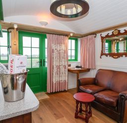 A room with a brown leather sofa a red wooden stool green doors and windows and a table with a metal ice bucket at Folklore in Bolton Percy near Tadcaster