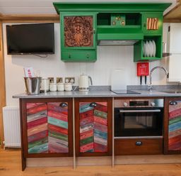 A kitchen with multicolored cabinet doors green upper cabinets a sink a stovetop an oven a TV mounted on the wall and a green door with stained glass at Folklore Bolton Percy near Tadcaster
