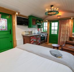 A room with a bed a kitchen area green doors and windows and a brown leather armchair at Folklore in Bolton Percy near Tadcaster