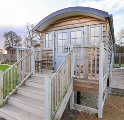 A small wooden cabin with steps leading to a porch with chairs and a table at The Fenton in Bolton Percy near Tadcaster