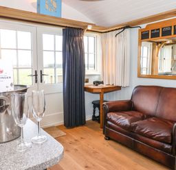 A room with a brown leather sofa a small wooden table and a window with dark and white curtains at The Fenton in Bolton Percy near Tadcaster