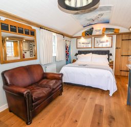 A bedroom with a leather sofa, a bed, and framed airplane pictures at The Fenton in Bolton Percy near Tadcaster
