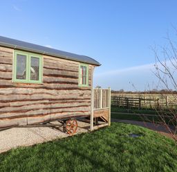 A wooden cabin with green framed windows and a small porch outside on grass at The Egyptologist in Bolton Percy near Tadcaster