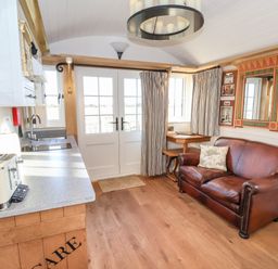 A kitchen and sitting area with a brown leather sofa and a small table near French doors at The Egyptologist in Bolton Percy near Tadcaster