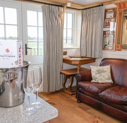 A room with a brown leather sofa next to a corner wooden table and two champagne glasses with a champagne bottle in an ice bucket on a countertop at The Studio in Bolton Percy near Tadcaster