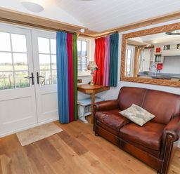 A room with a brown leather sofa colorful curtains a wooden desk with a lamp and double glass doors at The Studio in Bolton Percy near Tadcaster