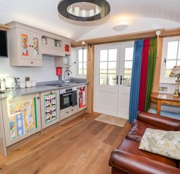A kitchen area with painted cabinets and a brown leather sofa near a wooden table with a lamp at The Studio in Bolton Percy near Tadcaster