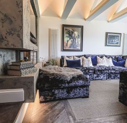 A living room with a sectional sofa with cushions a textured fireplace and framed wall art at Whisk Away Cottage Greystoke near Troutbeck Near Penrith