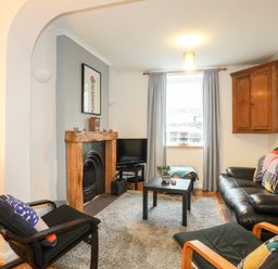 A living room with a black leather sofa and chairs a wooden fireplace a small black coffee table and a window with grey curtains at 5 Thomas Street in Llanberis