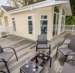 An outdoor deck with four chairs and a table with a bottle and four glasses at Seacroft in Stepaside near Kilgetty