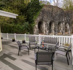 An outdoor deck with chairs a table with a bottle and glasses overlooking a stone wall and greenery at Seacroft in Stepaside near Kilgetty