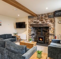 A living room with grey sofas a stone fireplace with a wood burner a wooden coffee table and a wall mounted television at Pennant Igyn in Mynytho near Abersoch