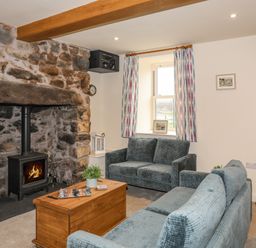 A living room with a stone fireplace and wood burning stove two sofas a wooden coffee table and patterned curtains at Pennant Igyn in Mynytho near Abersoch