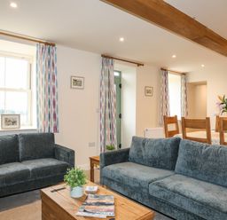 A living room with two sofas a wooden coffee table with plants and magazines a dining table with chairs and flowers on it at Pennant Igyn in Mynytho near Abersoch