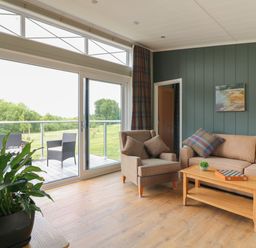 A living room with armchair sofa coffee table and plant next to large windows at Holly Lodge in Winthorpe near Newark-On-Trent