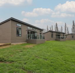 Three modern single-story cabins with glass balcony railings on a grassy area at Holly Lodge Winthorpe near Newark-On-Trent