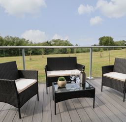 An outdoor seating area with two single chairs a two-seater sofa a glass-top table with wine glasses a bottle and a plant on a deck with glass railing at Cedar Lodge in Newark-On-Trent