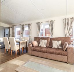 A living room with a brown sofa and patterned curtains near a dining table with four chairs at Orion in Felmoor Park