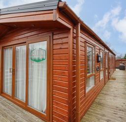 An exterior view of a wooden cabin with large glass doors and windows on a wooden deck at Orion in Felmoor Park
