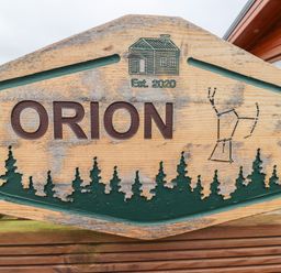 A carved wooden sign with the word Orion trees an outline of a cabin and a constellation at Orion in Felmoor Park