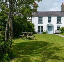 A garden with a wooden picnic table and a path leading to a white house at Tros Yr Afon in Beaumaris