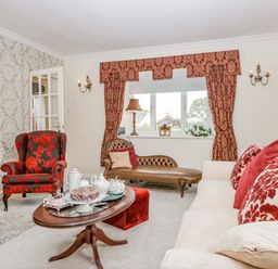 A living room with red patterned curtains a leather chaise lounge a red and black armchair a cream sofa with red patterned cushions and a wooden coffee table with tea set at Storrs Lodge in Bowness-On-Windermere
