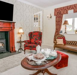 A living room with a fireplace armchair chaise lounge coffee table and window at Storrs Lodge in Bowness-On-Windermere