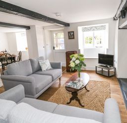 A living room with grey sofas wooden coffee table flowers on table and a small tv at Lime Cottage in Burton Bradstock
