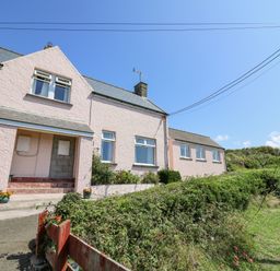 A row of pink houses with windows and doors next to green bushes and a clear blue sky at 2 Sunny Hill in Porthgain near St Davids