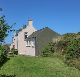 Exterior side view of houses with grass lawn and bushes under a clear blue sky at 2 Sunny Hill in Porthgain near St Davids