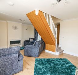 A living room with grey sofas a TV a fireplace blue rugs and a staircase at 2 Sunny Hill in Porthgain near St Davids