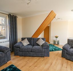 A living room with three dark gray sofas two rugs a glass side table with flowers and blue patterned curtains at 2 Sunny Hill in Porthgain near St Davids