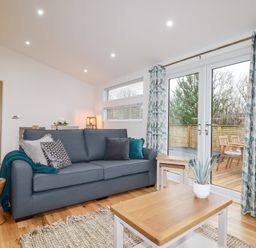 A living room with a gray sofa and patterned curtains next to glass doors showing an outdoor deck at 7 Valley View in Lanreath