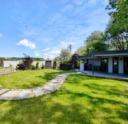 A garden with a curved stone pathway leading to a white building with a covered patio at Sanderson House in Cleator Moor