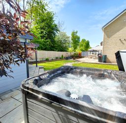An outdoor hot tub bubbling on a patio next to a garden and a house at Sanderson House in Cleator Moor