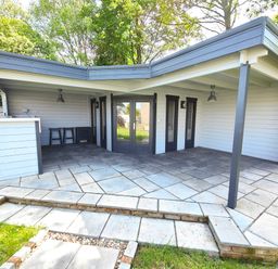 An outdoor covered patio area with a bar counter two stools and dark framed glass doors at Sanderson House in Cleator Moor