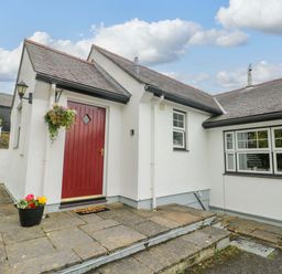 A house entrance with a red door and flower pots at Bwthyn Clai in Llangefni