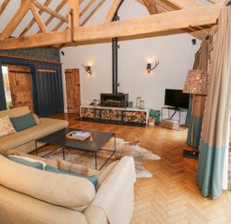 A living room with exposed wooden beams a wood burning stove and beige sofas at Fairoaks Barns in Hollybush near Ledbury