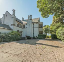 An exterior view of a white multi-story house with chimneys surrounded by trees at Highcliffe Manor in Flamborough