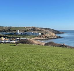 A coastal landscape with a large building near a beach and green fields at The White House in Weymouth