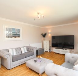 A living room with two grey sofas a large flat screen TV a white side table and wooden bookshelf at The White House in Weymouth