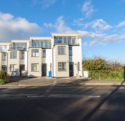 A row of three story modern white houses with balconies and a road in front at Chy Fistral in Newquay